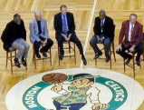 Five guys sitting on chairs next to Celtics logo on the parquet floor waiting to tell stories