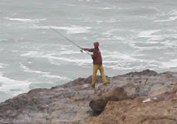 Closeup of a person in a red jacket on the rock casting a fishing line